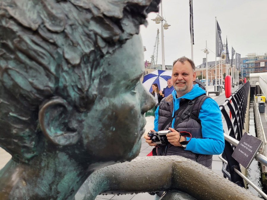 Ein Tourist steht mit der Kamera in der Hand vor einer Statue. 