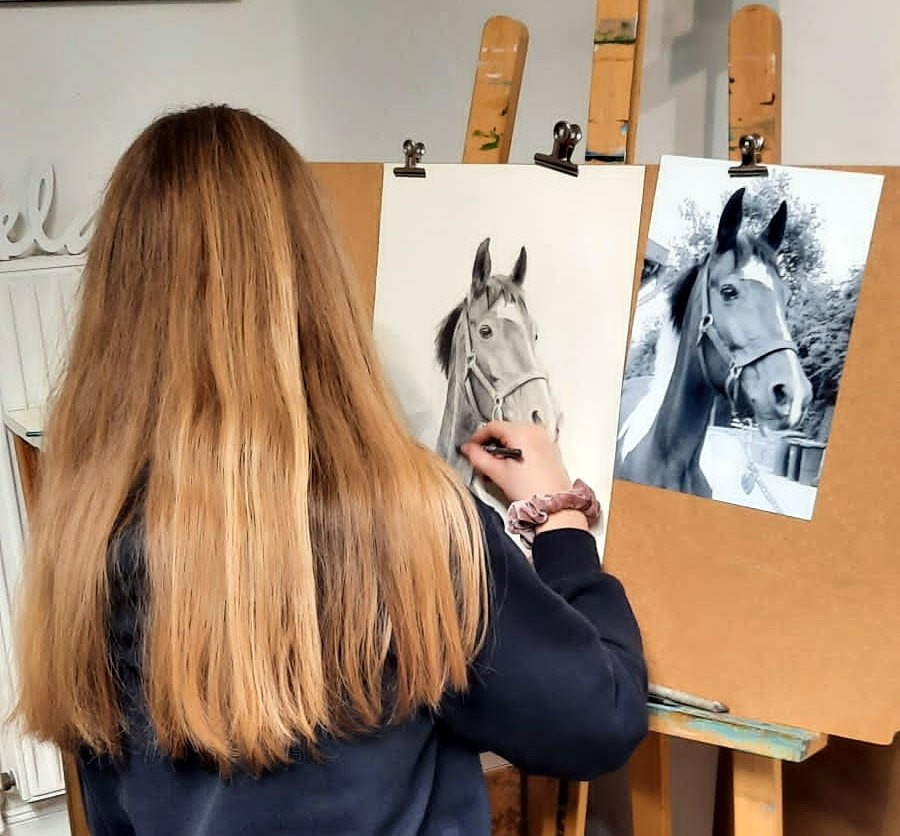 Eine junge Frau zeichnet ihr Pferd mit einem Foto als Vorlage.