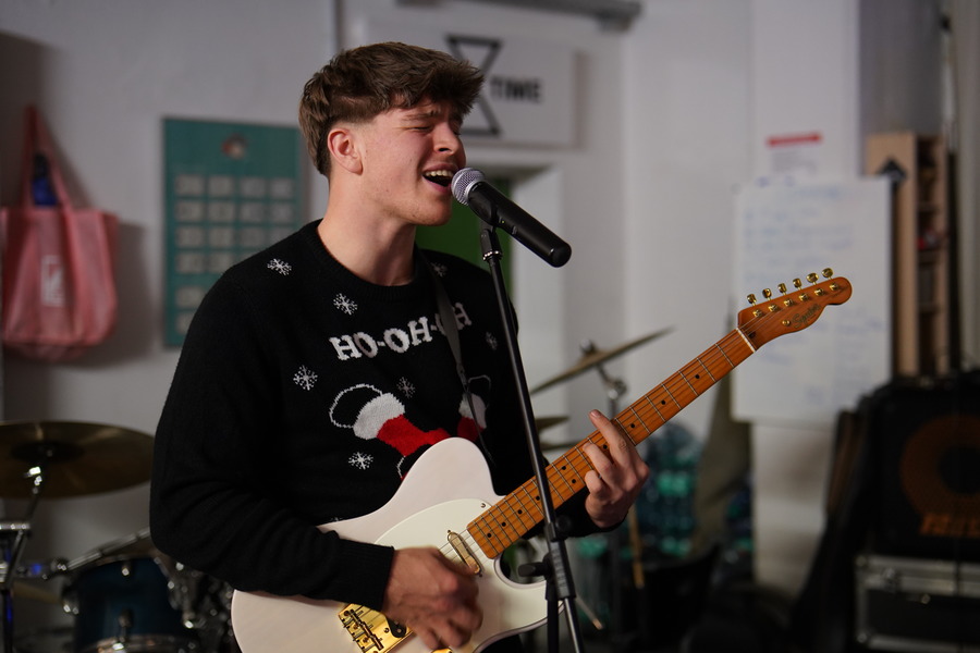 Ein junger Mann singt ins Mikrofon und spielt gleichzeitig Gitarre. 