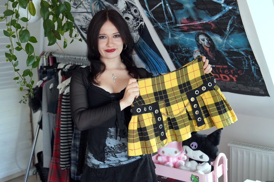 Eine junge Frau hält einen gelbschwarz karierten Rock hoch. 