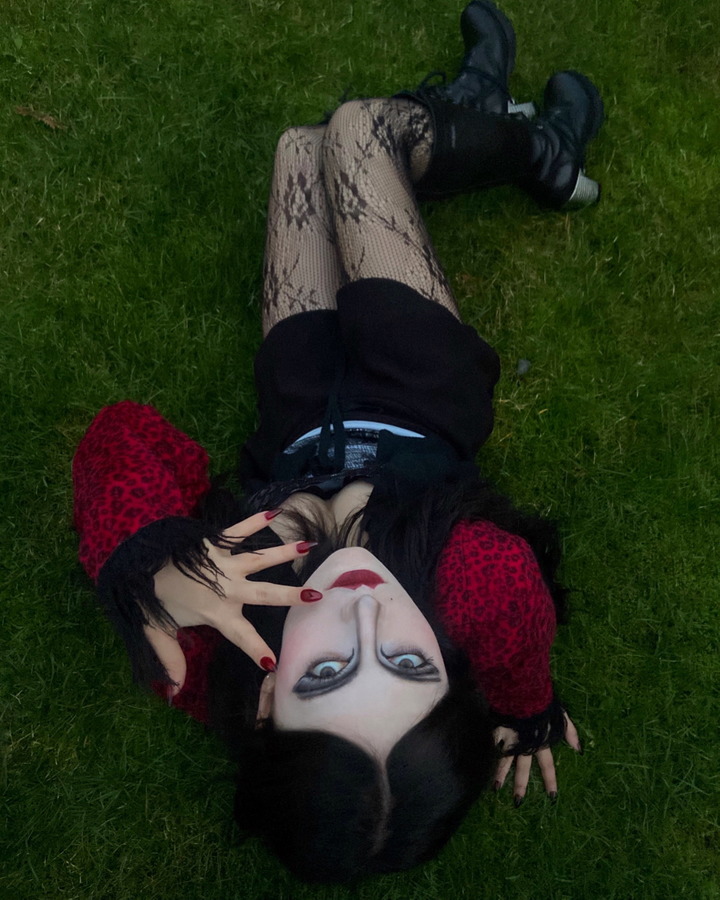 Eine junge Frau im Goth-Look liegt auf einer Wiese und wird über Kopf abgebildet. 